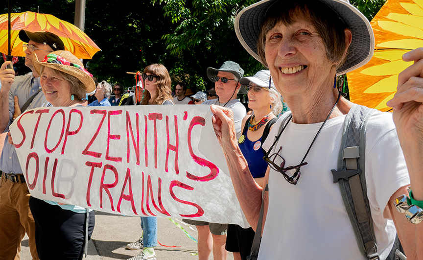 Activist holding a small banner that says, "Stop Zenith Oil Trains".